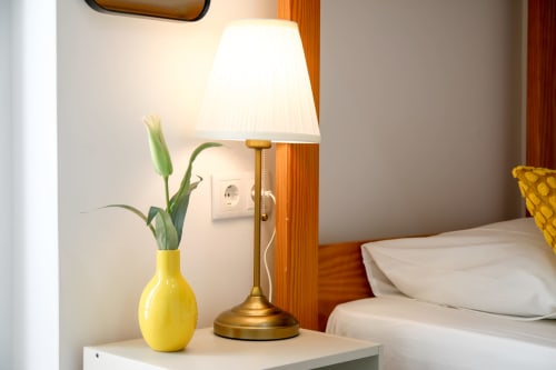 Bedside table with yellow vase, green plant, and brass lamp in Lisbon Poets Inn hostel room