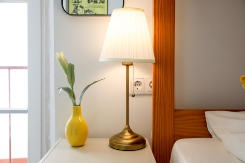 Bedside table with brass lamp, yellow vase with plant, and wall outlet at Lisbon Poets Inn hostel