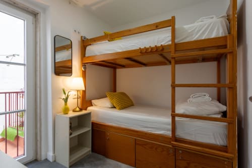 Wooden bunk bed with white linens in Lisbon Poets Inn hostel room, featuring bedside lamp and balcony access