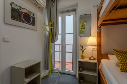 Cozy double room at Lisbon Poets Inn hostel with wooden bed, yellow accents, balcony overlooking water, and modern amenities