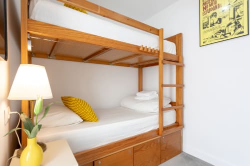 Wooden bunk bed with white bedding and yellow pillow in Lisbon Poets Inn hostel room, with lamp and plant on nightstand