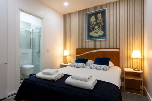 Modern bedroom suite at Lisbon Poets Inn hostel with wooden bed, white linens, blue pillows, ensuite bathroom, and