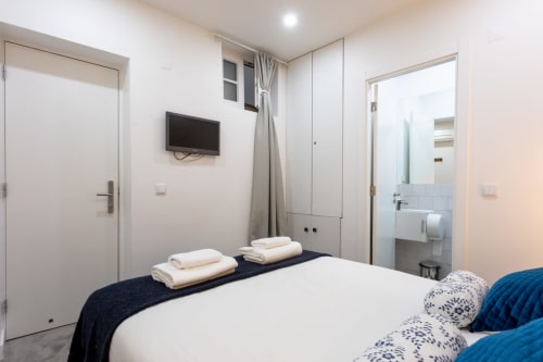 Lisbon Poets Inn hostel Suite Casal bedroom with white bed, dark bedding, wall-mounted TV, and ensuite bathroom