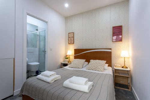Lisbon Poets Inn suite with brown headboard, white bedding, ensuite bathroom, patterned wallpaper, and ambient lighting.
