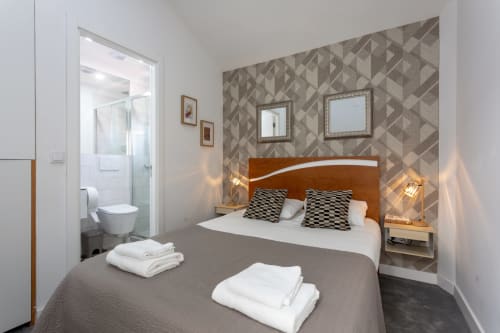 Modern bedroom suite at Lisbon Poets Inn hostel with wooden headboard, patterned accent wall, and ensuite bathroom