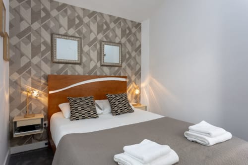 Modern suite bedroom at Lisbon Poets Inn with wood headboard, patterned wallpaper, mirrors, and fresh white towels