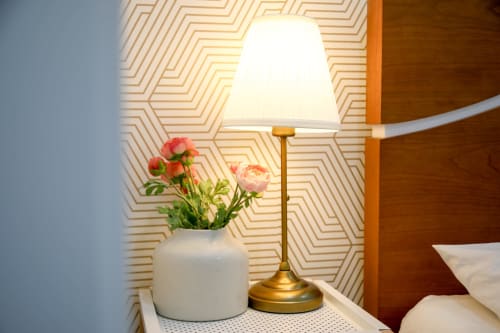Bedside table at Lisbon Poets Inn with pink flowers, brass lamp, and patterned wallpaper in Suite Casal room