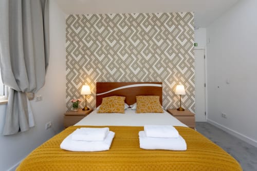 Lisbon Poets Inn double bedroom with geometric patterned headboard, yellow bedding, and twin bedside lamps