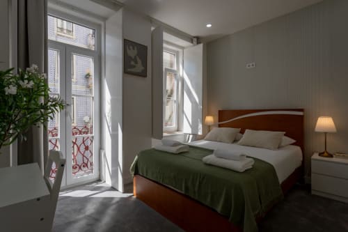 Bright bedroom at Lisbon Poets Inn with double bed, green bedding, wooden headboard, and doors opening to balcony with city