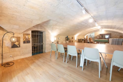 Salle à manger souterraine du Pavillon Des Millésimes avec voûte en pierre, table en bois et chaises blanches