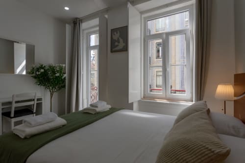 Bright double bedroom at Lisbon Poets Inn with green accent bed, large windows, desk, mirror, and modern minimalist décor.