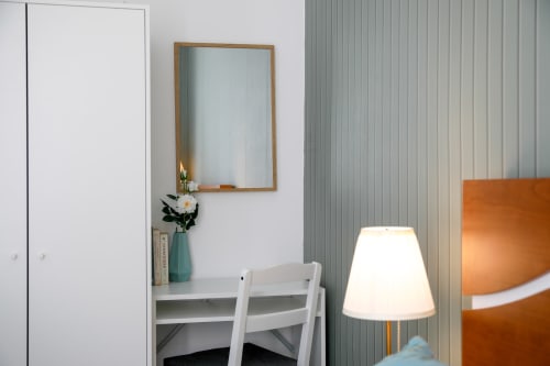 Modern hostel room corner with desk, white chair, wooden mirror, teal vase with flowers, and table lamp at Lisbon Poets Inn