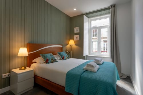 Cozy double bedroom at Lisbon Poets Inn with wooden bed, teal accents, green striped walls, and window view