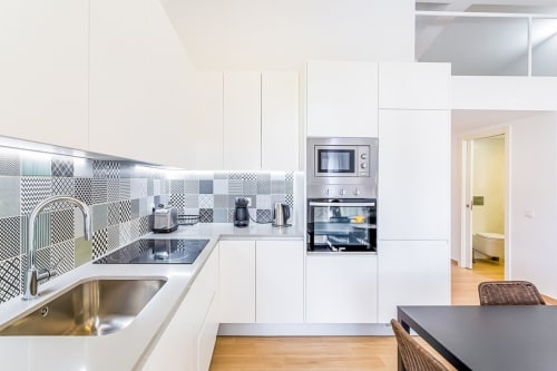 Cozinha moderna branca com azulejos estampados em preto e branco, pia de aço inoxidável, forno embutido e micro-ondas no Barracuda