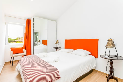 Quarto moderno com cabeceira laranja, roupa de cama branca, piso em madeira e decoração contemporânea na Algarve Beach Holidays