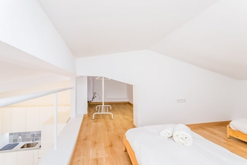 Quarto estilo loft moderno no apartamento Barracuda, Algarve, com assoalho em madeira, paredes brancas e móveis contemporâneos