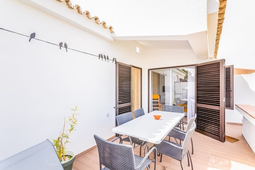 Moderna zona de refeições na varanda do apartamento Barracuda na Praia do Algarve, com mesa branca, cadeiras cinzentas e portas com vista para o oceano