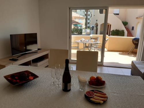 Sala de jantar moderno de apartamento no Algarve com terraço vista para o oceano, garrafa de vinho, frutas frescas e sala de TV