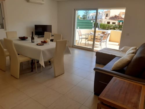 Sala de estar do apartamento MARSOL com mesa de jantar, sofá, TV e terraço com vista para casarões do Algarve