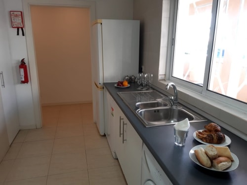 Cozinha do apartamento MARSOL na Praia do Algarve com pia em aço inoxidável, armários brancos, itens para café da manhã e vista para a cidade