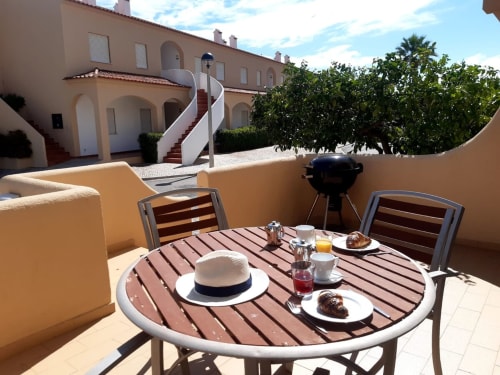 Terraço ensolarado do apartamento MARSOL na praia do Algarve com mesa de jantar, chapéu e vistas para vilas costeiras