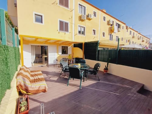 Terraço ensolarado do apartamento Algarve Beach Holidays com mesa de jantar, espreguiçadeiras e edifício amarelo na Praia da Bottelha,