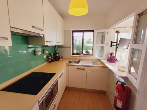 Cozinha moderna em apartamento de férias na Praia do Algarve com backsplash verde, bancadas de madeira e luminária pendente amarela vibrante