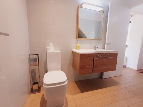 Banheiro moderno em apartamento no Algarve com gabinete em madeira, vaso sanitário branco e espelho em Praia da Bottelha