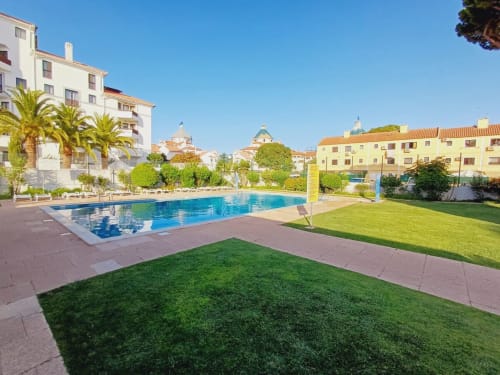 Piscina ensolarada do Algarve Beach Holidays com espreguiçadeiras, palmeiras e edifícios tradicionais portugueses em Praia