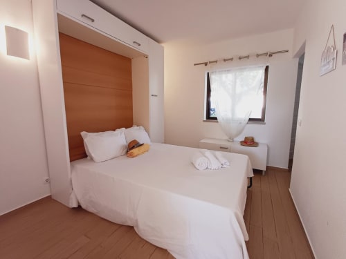 Quarto luminoso com roupa de cama branca, cabeceira laranja e piso de madeira no apartamento Algarve Beach Holidays em Praia da