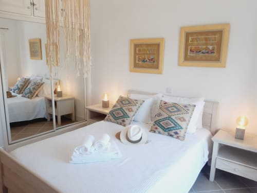 Quarto elegante em apartamento na Praia do Algarve com roupa de cama branca, almofadas padrão geométrico, quadros na parede e vista para o mar