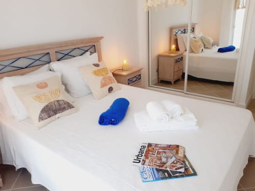 Quarto luminoso de apartamento de praia em Algarve Beach Holidays com cama de madeira, almofadas decorativas, toalhas enroladas e espelho