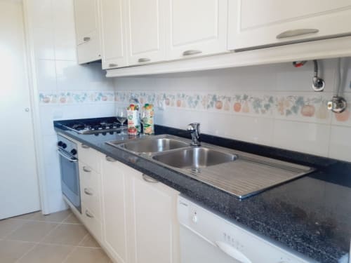 Cozinha moderna no apartamento VILLALUSA na Praia do Algarve com armários brancos, bancada escura e aço inoxidável