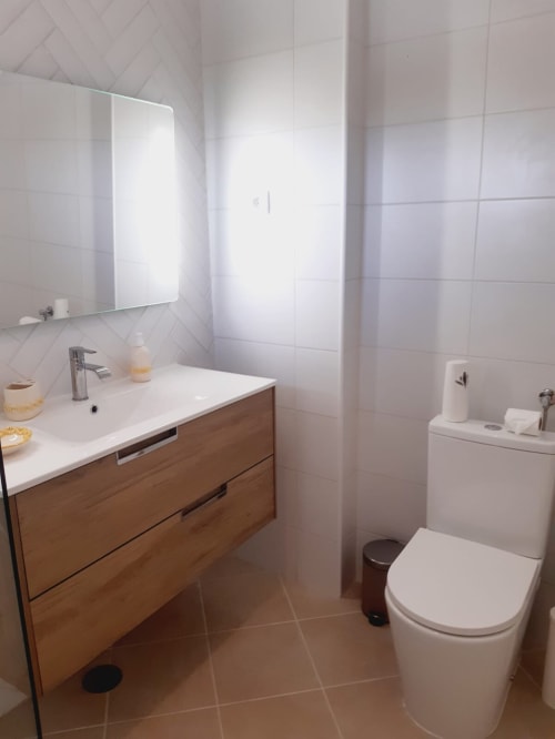 Banheiro moderno do apartamento VILLALUSA Beach com gabinete em madeira, azulejos brancos, vaso sanitário e espelho iluminado