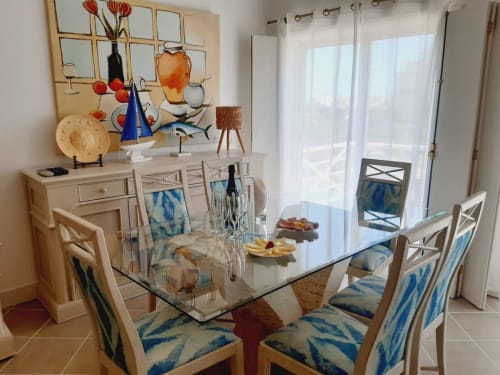Sala de jantar luminosa no apartamento de praia VILLALUSA no Algarve com mesa de vidro, cadeiras com padrão azul e vista para o oceano