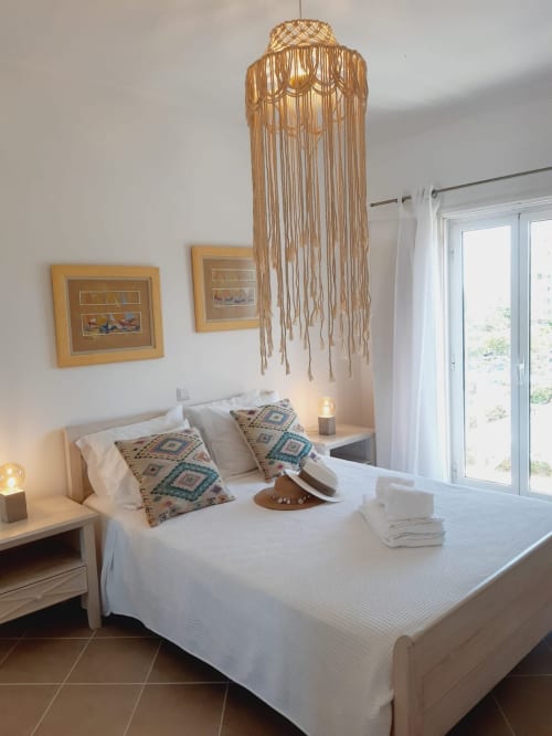 Quarto luminoso do apartamento no Algarve com cama branca, painel de macramé, arte emoldurada e portas para varanda com vista para piscina