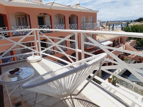 Terraço ensolarado do apartamento de praia VILLALUSA no Algarve com espreguiçadeira branca, rede e vista para edifícios em tons de terracota