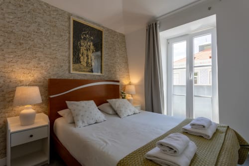 Bright bedroom at Lisbon Poets Inn with double bed, cork wallpaper, wooden headboard, and glass doors overlooking city