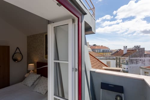 Lisbon Poets Inn room with bed, balcony view of terracotta roofs, and modern white glass door in Lisboa