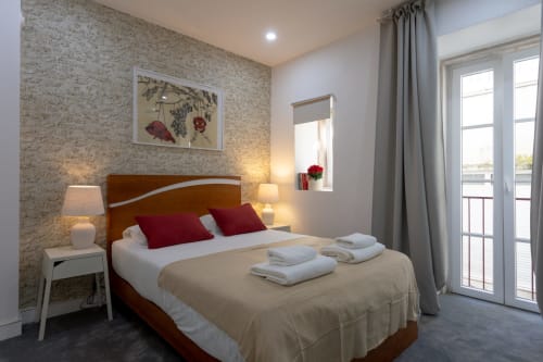 Suite Casal bedroom at Lisbon Poets Inn with wooden bed, red pillows, stone accent wall, and balcony access