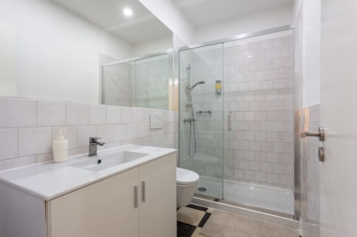 Modern bathroom in Lisbon Poets Inn hostel with white subway tiles, glass shower enclosure, vanity sink, and toilet