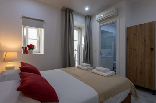 Modern bedroom suite at Lisbon Poets Inn with queen bed, red pillows, ensuite bathroom, air conditioning, and natural light