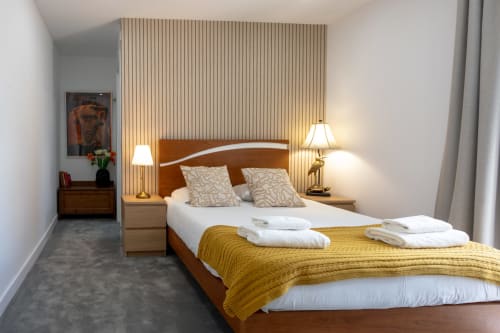 Modern hotel bedroom at Lisbon Poets Inn with wooden bed frame, golden bedding, white pillows, side lamps, and vertical