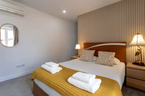 Modern Suite Casal bedroom at Lisbon Poets Inn with queen bed, mustard throw, white towels, wooden furniture, and striped