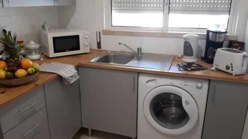 Cozinha moderna no apartamento de praia MARESIA, Algarve, com balcões de madeira, pia, máquina de lavar e eletrodomésticos