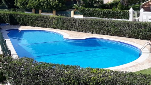 Piscina curvilínea de luxo com água azul-turquesa na Algarve Beach Holidays, cercada por sebes aparadas e pedra