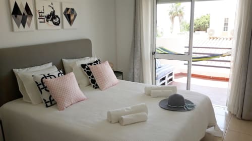 Quarto moderno no apartamento Maresia em praia do Algarve com cabeceira cinzenta, almofadas rosa, toalhas enroladas e vista para terraço