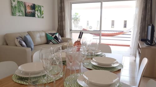 Área de refeições do apartamento Maresia com mesa posta, sofá bege e varanda com vista para a cidade do Algarve
