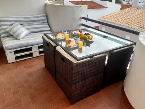 Terraço na cobertura do apartamento de praia Maresia com setup de café da manhã, móveis de vime e vista da cidade do Algarve