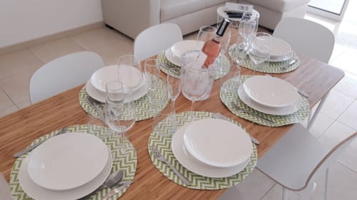 Elegante mesa de jantar no apartamento de praia Maresia no Algarve com pratos brancos, passadeiras verdes e copos de água